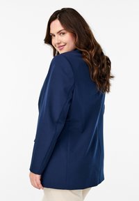 Laivansinis bleiseri, jossa on rakenteellinen muotoilu, pitkät hihat ja sileä pinta. Varustettu yksittäisellä napilla ja ilman näkyviä kuvioita.