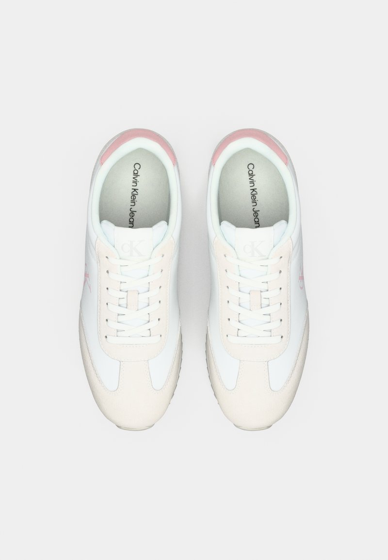 Une paire de baskets blanches Calvin Klein avec des accents rose pâle, fermeture à lacets, et logo visible sur les semelles intérieures et sur les côtés.