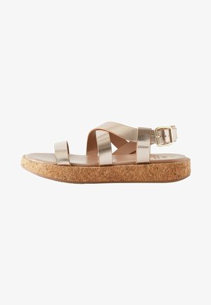 Sandalias metálicas doradas con tiras anchas cruzadas, suela de corcho y hebilla ajustable en la correa del tobillo. Textura suave.