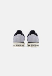 Sneaker in tela grigia chiara con design a basso taglio, suole in gomma bianca e dettagli neri sul tallone con il logo "CONVERSE ALL STAR".