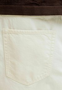Poche arrière en denim blanc avec un motif de vague cousu subtil et une ceinture en tissu brun au-dessus.
