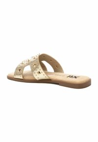 Sandalias deslizantes beige con tachuelas doradas en forma de pirámide, con un diseño de tiras cruzadas y una plantilla texturizada en tono marrón, suela de goma plana.
