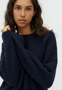 Marineblauer, gerippter Strickpullover mit weiten, übergroßen Ärmeln und Rundhalsausschnitt, der ein strukturiertes Muster und eine weiche Haptik aufweist.