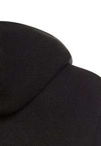 Zwarte gebreide hoodie met een textuurstof, voorzien van een strakke capuchon en ribbels aan de randen, vastgelegd vanuit een hoek om de stiknaden te benadrukken.