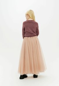 Falda larga de tul plisada y translúcida en un suave tono rosa con toques brillantes, combinada con un suéter ajustado de texturizado burdeos y zapatos negros.