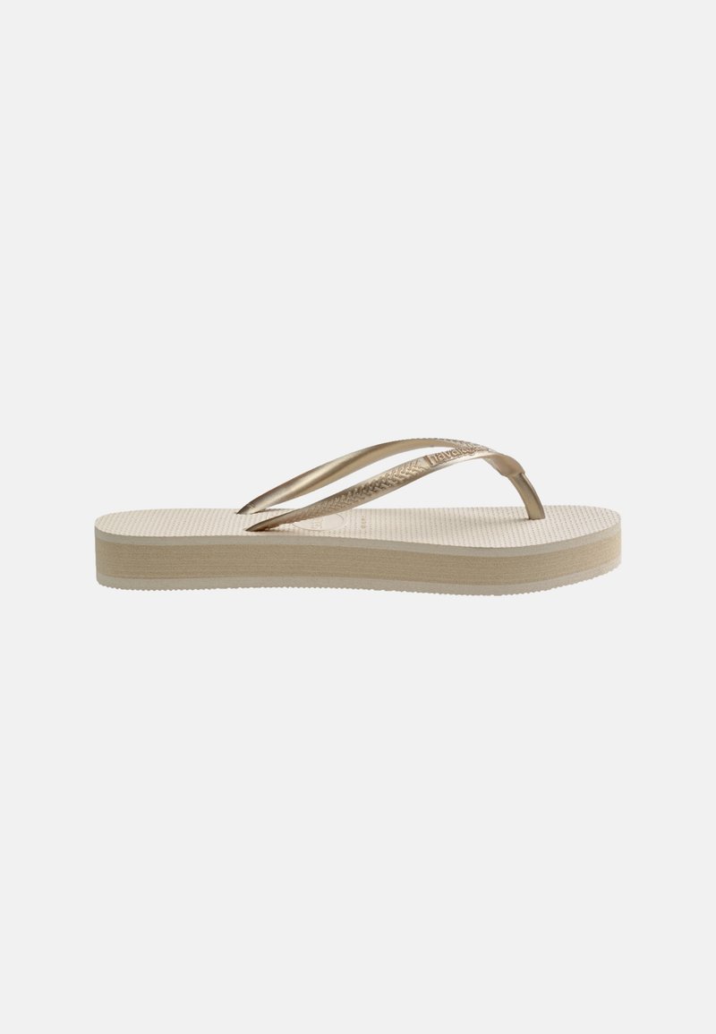 Sandale tongs beige avec semelle texturée et bride en forme de Y métallique dorée sur fond blanc.