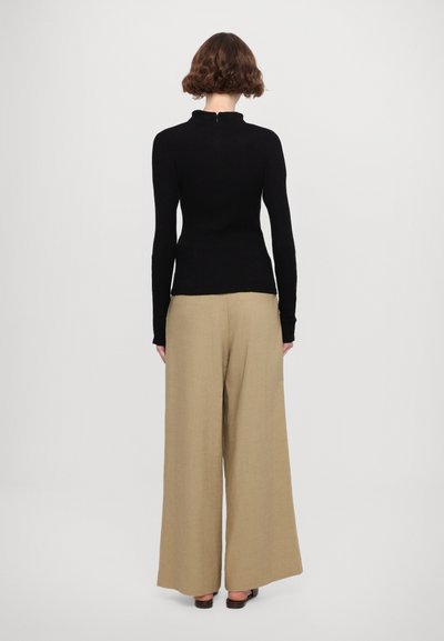 Black fitted sweater with a high collar and zip closure, paired with wide beige trousers made from a textured fabric.