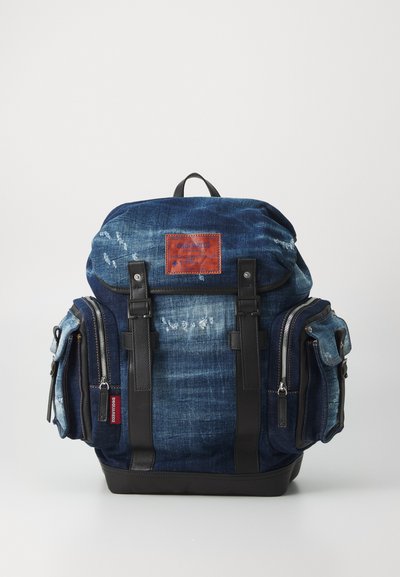 Denim-Rucksack mit strukturierter Form, dunkler blauer Farbe, Lederakzenten, Fronttaschen und Metallreißverschlüssen, mit einem markierten Lederpatch.