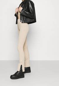 Svart läder kort jacka, beige ribbade leggings med slits i nederkant, parat med chunky svarta plattformsskor. Enkel, strömlinjeformad design.