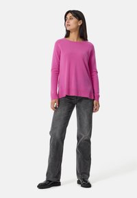 Maglione rosa a maniche lunghe in una texture morbida con una vestibilità rilassata. Indossato con jeans grigio scuro e scarpe nere. Design semplice e casual.
