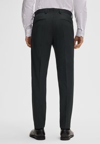 Donkergroene op maat gemaakte broek met een gladde textuur, slim fit en twee achterzakken. Gecombineerd met een witte overhemd met lange mouwen en zwarte schoenen.
