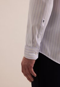 Lichtblauw en wit gestreept shirt met een knopmanchet en geborduurd detail op de mouw. De stof heeft een gladde textuur en een aangesloten ontwerp.