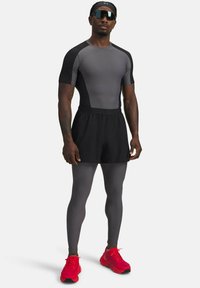 Athletischer Mann in grauen Kompressionsleggings und -shirt, schwarzen Shorts, roten Laufschuhen, schwarzem Stirnband und großen schwarzen Sportsonnenbrillen.