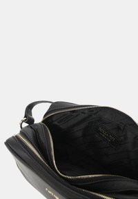 Borsa a tracolla in pelle nera con dettagli della cerniera dorati. L'interno presenta una fodera decorata e un'etichetta. Design compatto con una sola tracolla.