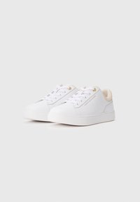 Hvite lave sneakers med hvite snøringer, gull maljer, beige indre fôr og "Tommy Hilfiger"-logo på siden.