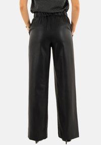 Pantalons larges noirs avec une texture lisse et brillante, taille élastique et deux poches arrière. Le design est décontracté et ample.