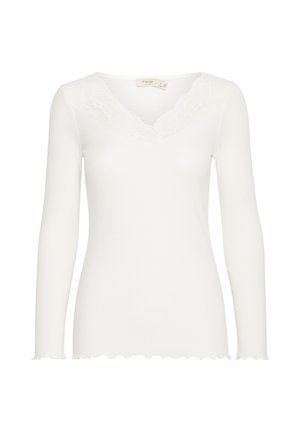 Haut blanc à manches longues avec une texture côtelée, arborant une encolure en V ornée de dentelle et de bords festonnés aux manches et à l'ourlet.