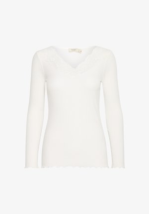 Valge pika varrukaga pluus, millel on ribakujuline tekstuur, V-kaelus, mis on kaunistatud pitsäärtega ja laineliste äärtega varrukatel ja alushelil.