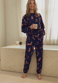 Navy loungewear set met hondenpatronen; lange mouwen top en broek met elastische tailleband. Zachte stof, relaxte pasvorm en ribgebreide manchetten.