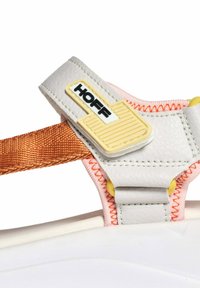 Zapatilla blanca con una correa texturizada en gris, acentos naranjas, herrajes amarillos y un logo negro "HOFF". Presenta costuras reforzadas.