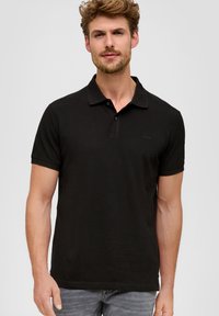 Zwarte polo met een klassiek kraag, korte mouwen en een subtiele logodetail op de borst; gemaakt van een zachte stof; een schone uitstraling.