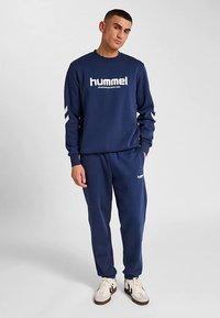 Marinblå sporttröja med vitt varumärke, kombinerad med matchande marinblå joggingbyxor. Har vita detaljer längs ärmarna och mjuk tygstruktur.