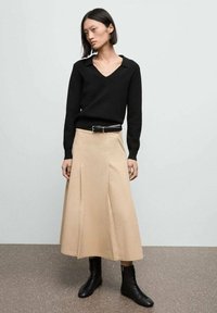 Schwarzer V-Ausschnitt-Pullover, beiger Plisseerock und schwarze schnürbare Ankle-Boots. Glatte Texturen und taillierte Passform mit einer definierten Taille.