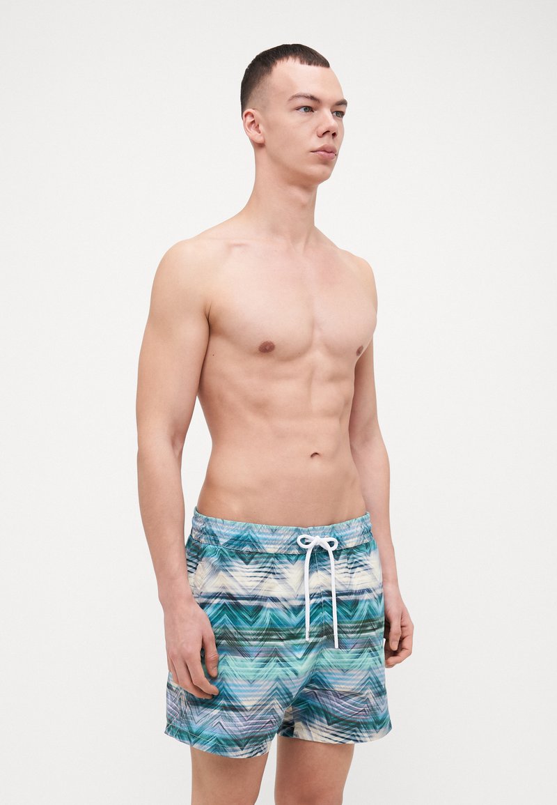 Men's swim shorts in a multicolored, wavy pattern of blues and greens. Elastic waistband with a drawstring. Lightweight, quick-drying material.
