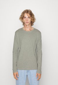 Langermet t-skjorte i lysegrått stoff, rund hals, avslappet passform, med teksturert overflate og subtile sømdetaljer. Sammen med lyseblå jeans.