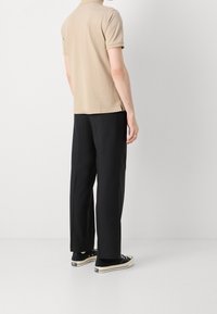 Beige polo-shirt med korte ærmer, parret med sort brede bukser. Har sideslids og sorte sneakers med hvide detaljer.