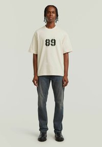 Crème t-shirt met gedurfde zwarte "89" opdruk op de voorkant; relaxed fit. Gecombineerd met vervaagde blauwe jeans en zwarte laarzen. Structuur van katoen.