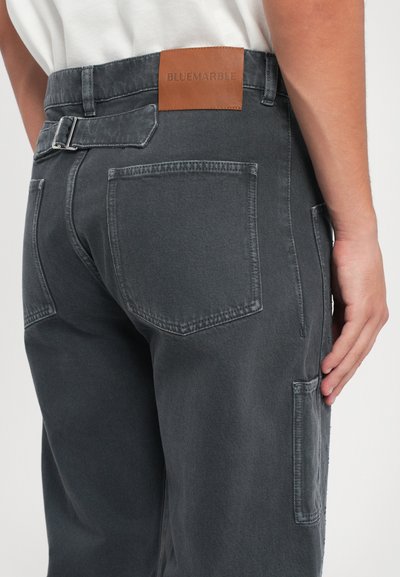 Grijze denim broeken met een leren label "BLUEMARBLE," zijzakken en een gespdetail bij de taille. Zachte textuur, modern design.