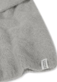 Couverture en laine grise avec une surface douce et texturée. Dispose d'une petite étiquette en tissu le long du bord avec un texte imprimé.