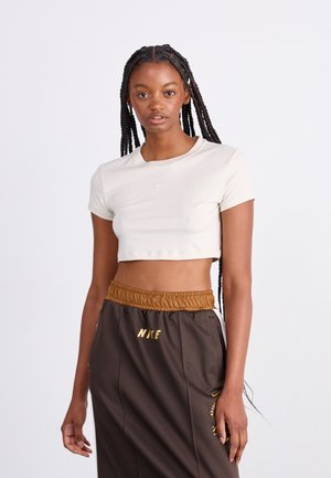 Cream short-sleeve cropped t-shirt with a round neckline and Nike logo paired with brown pants featuring an elastic waistband and branding accents.