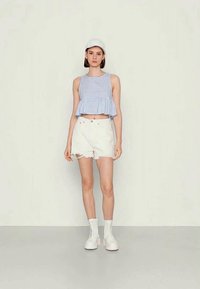 Top cropped em xadrez azul claro com bainha em babados, combinado com calções brancos desgastados. Botas de cano baixo brancas com atacadores e um boné branco completam o visual.