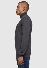 Grauer Rollkragenpullover mit langen Ärmeln, geripptem Kragen und Bündchen; taillierter Schnitt mit glatter Textur. Getragen mit blauen Jeans.