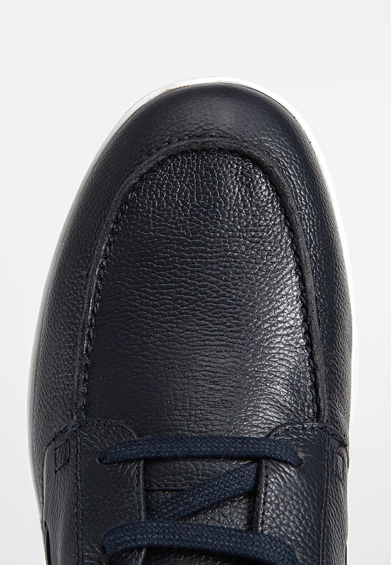 Chaussure en cuir marine avec finition texturée, bout arrondi et lacets navy. Elle dispose d'une semelle en caoutchouc blanc et d'un discret détail de couture.