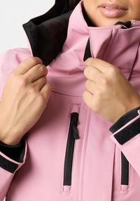 Giacca rosa con colletto alto, tasche con zip e dettagli neri. Il materiale appare liscio, con una consistenza morbida e una costruzione resistente.