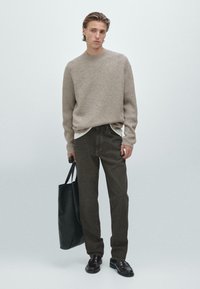 Beige ribbet trøje over en hvid skjorte, brune lige ben bukser, sort tote taske og sorte sko, sat mod en ensfarvet lys baggrund.