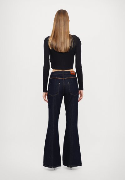Jeans acampanados de color azul oscuro con una cintura alta, que cuentan con una etiqueta de marca naranja, cinco bolsillos y costuras en contraste en la parte trasera.