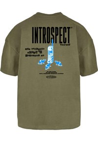 Olīvu zaļš pārmērīgi liels T-krekls ar grafisku apdruku uz muguras: zils retro telefons ar tekstu "INTROSPECT Yourself" un citiem frāzēm.