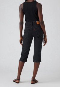 Pantalones capri de mezclilla negra con cintura alta, cinco bolsillos y una etiqueta de marca de cuero. Textura lisa y detalle de dobladillo vuelto.