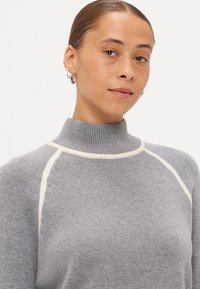 Γκρι πλεκτό πουλόβερ με ψηλό  ribbed γιακά, διακοσμημένο με εκρού ραφή κατά μήκος των ώμων και της λαιμόκοψης. Μαλακή υφή.