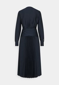Robe longue noire à manches longues, taille ajustée, tissu froncé au milieu du dos, et jupe plissée s'étendant jusqu'à mi-mollet, vue de dos.