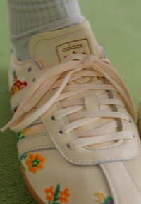 Adidas sneaker van crèmekleurig leer met bloemenborduursel in rood, oranje en groen. Heeft een gevoerde tong en textuurveters.