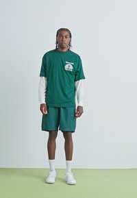 Grøn bomulds T-shirt med en hvid langærmet bluse under, parret med matchende grønne shorts. Båret med hvide sneakers og ankelsokker.