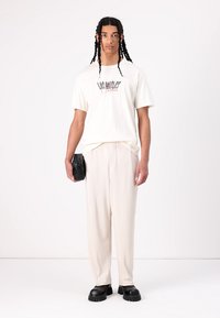Off-white t-shirt med "LOS ANGELES" grafik, parret med cremede plisserede bukser og chunky sorte sko. Holder en sort taske.