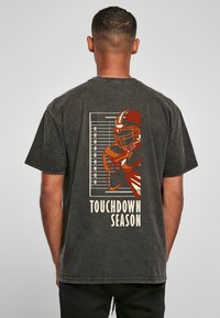 Čierne bavlnené tričko s grafikou futbalistu a textom "TOUCHDOWN SEASON" v béžovej farbe na zadnej strane, s opotrebovaným vzhľadom.