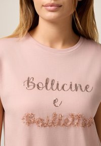 Rosa Baumwoll-T-Shirt mit kurzen Ärmeln, mit silbernen Pailletten-Schriftzug "Bollicine e Paillettes" in dekorativen Stilen auf der Vorderseite.