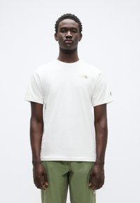 Άσπρη βαμβακερή μπλούζα με κοντά μανίκια, που έχει ένα μικρό κίτρινο λογότυπο στο αριστερό στήθος και επιπλέον σήμανση στο μανίκι.